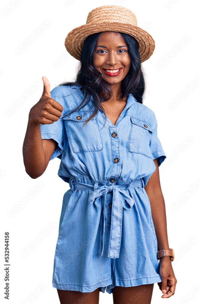 Young indian girl wearing summer hat doing happy thumbs up gesture with hand. approving expression looking at the camera showing success. Young indian girl wearing summer hat doing happy thumbs up gesture with hand. approving expression looking at the camera showing success.