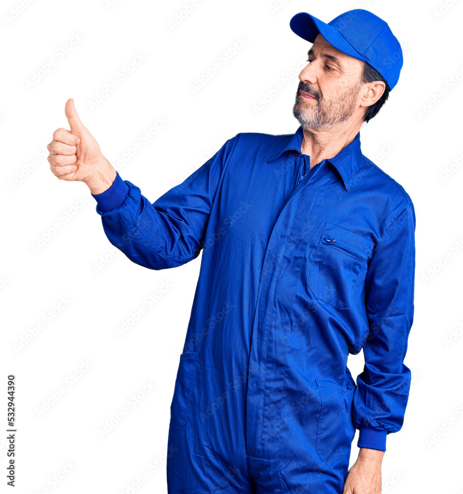 Middle age handsome man wearing mechanic uniform looking proud, smiling doing thumbs up gesture to the side Middle age handsome man wearing mechanic uniform looking proud, smiling doing thumbs up gesture to the side