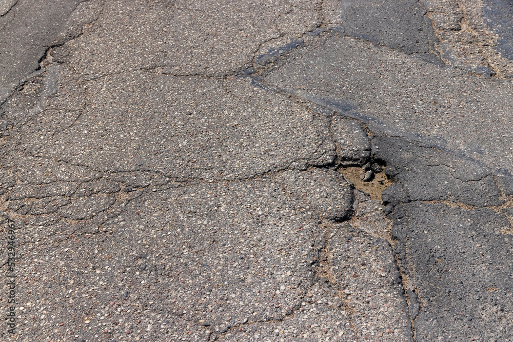 An old paved road with a lot of holes and damage An old paved road with a lot of holes and damage