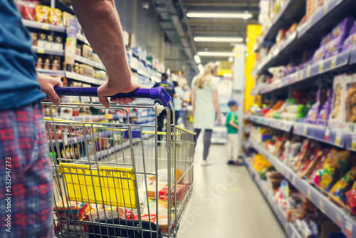 Man with a basket walks in a supermarket. Hand and part of the basket in focus, blurred background