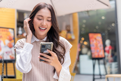 attractive asian woman pleased positive casual hand hold smartphone enjoy leisure relas sitting in front of street food booth corner in outlet department store mall relax shopping lifestyle concept photo