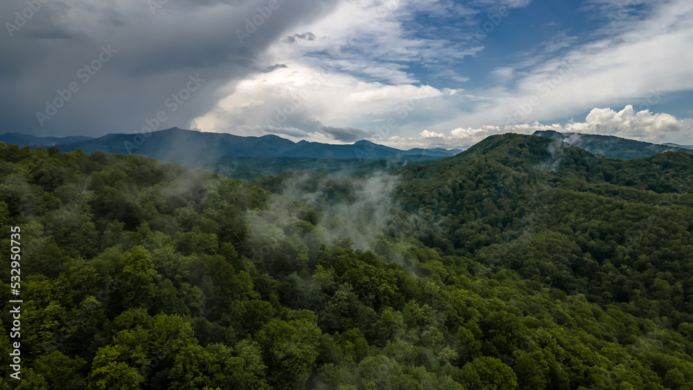 Beautiful nature in the mountains. Fog over the forests. Blue sky with clouds. Green trees on the slopes of the mountains. Mystical fog after the rain.