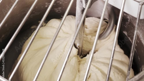 Dough for pizza or bread is kneaded in a dough mixer. The camera shoots from above through a metal grid