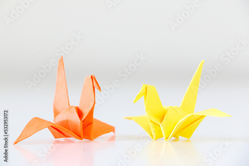 Two Japanese origami cranes facing each other, one orange, one yellow, on white background