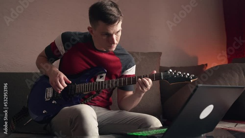 Young man learning to play electric guitar online using laptop. close-up