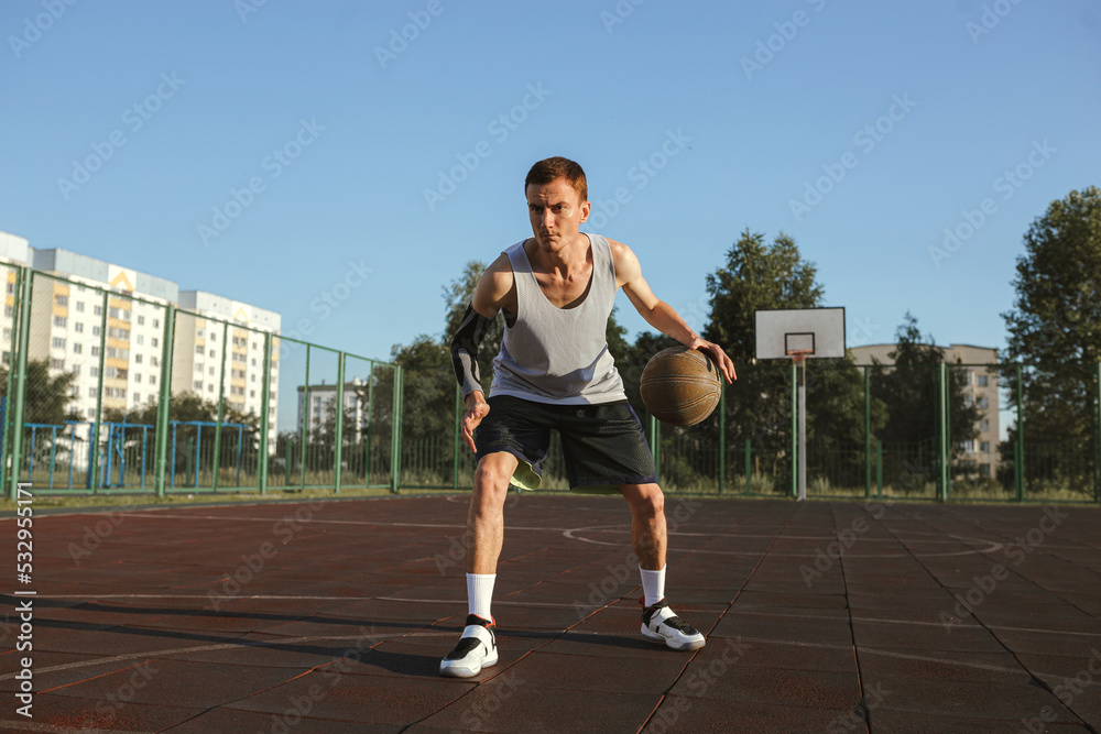 Full body of focused athletic man with basketball playing street ball on outdoors urban playground on sunny day in summer 