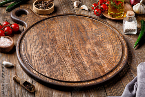 Empty round wooden cutting board for food, pizza. Menu, recipe Mock up. Wooden background with oil, tomatoes and spices. .