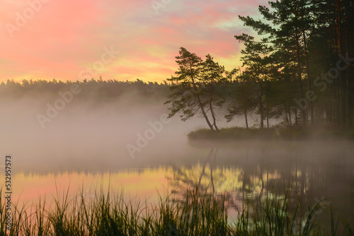 a wonderful sunrise picture with a gorgeous sky, fog covering the surface of the lake, black silhouettes of trees