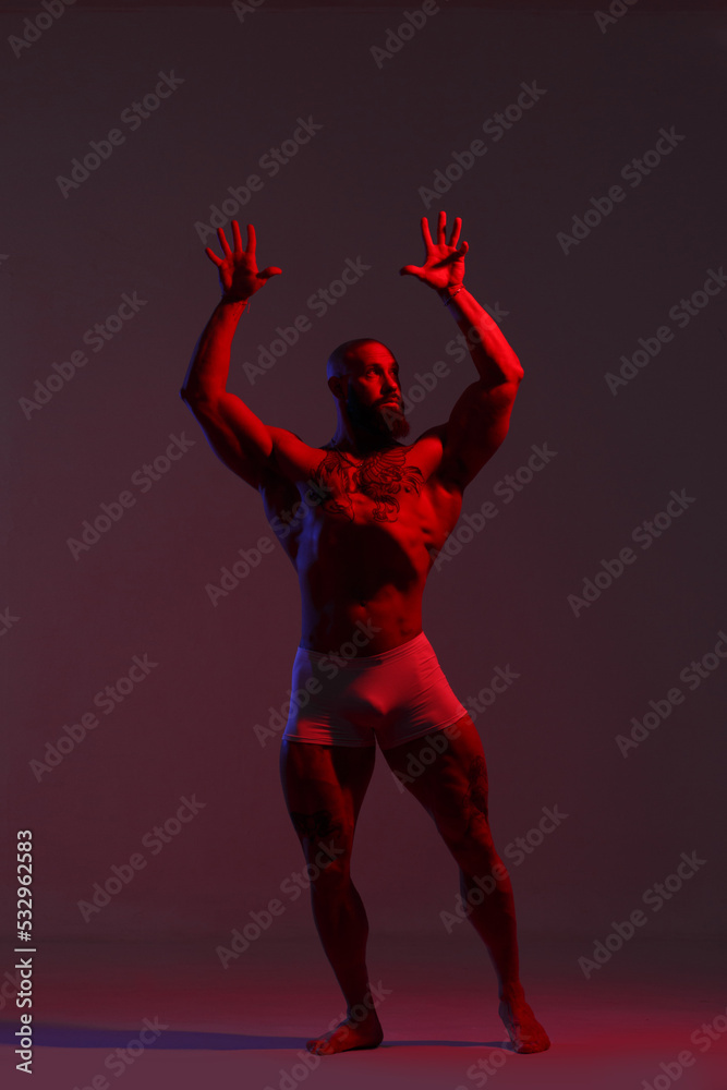 Athletic man demonstrates muscles in the light of a red light filter on a dark background.
