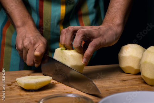 Working in the kitchen. Detail of hands cutting apple into pieces. Cutting board. Chef's knife. Dark black background.