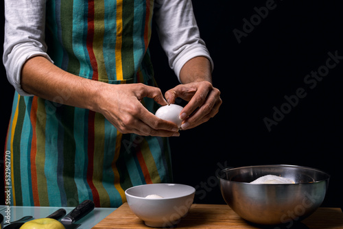 Working in the kitchen. Cracking an egg in a bowl. Cooking apple pie. Cook table. Dark black background.