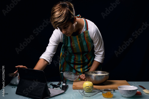 Working in the kitchen. Looking at recipe on website on tablet. Opening to cook. Cooking apple pie. Dark black background.