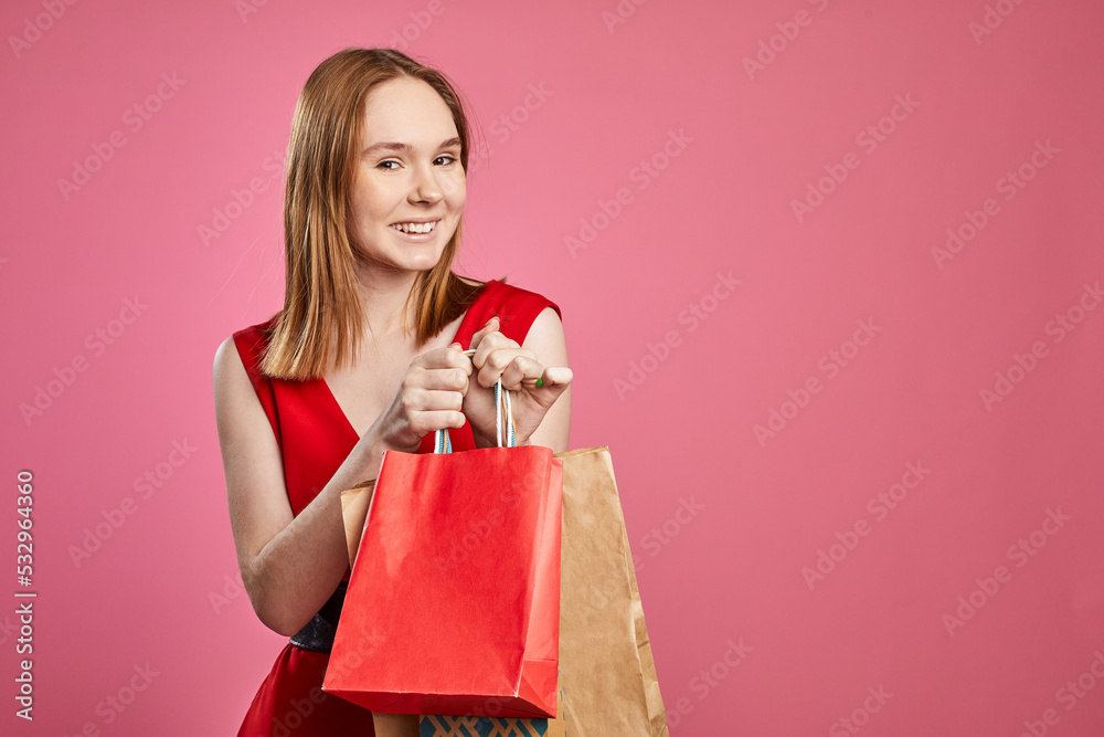 Young woman with happy positive smile wearing stylish red clothing excited hold shopping bags sale on pink background. Young woman with happy positive smile wearing stylish red clothing excited hold shopping bags sale on pink background.