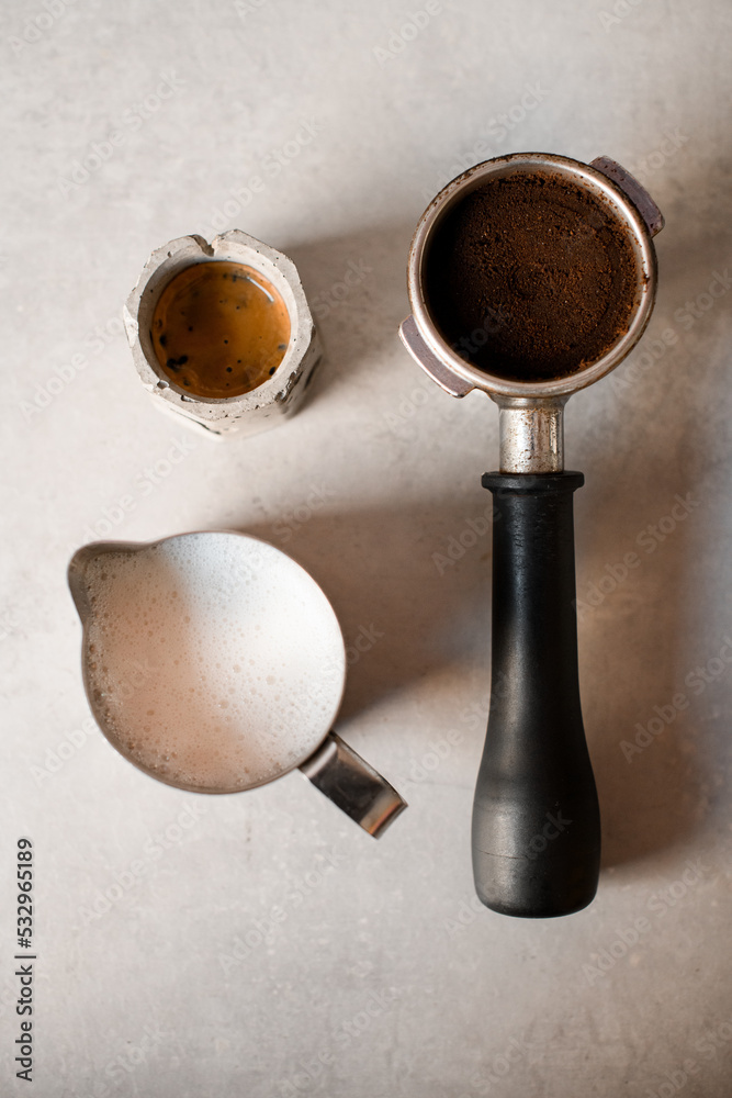 top view of holder with portafilter full of ground coffee and cup with drink and jug with milk