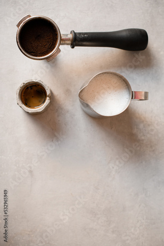 beautiful top view of holder with portafilter full of ground coffee and cup with drink and jug with milk