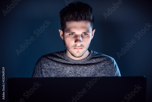 man at night in front of laptop look to screen with serious face while recognize he become a victim of scam