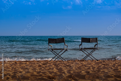 Two beach folding chairs on the seashore at sunset with a blue sea and a colorful sky. Travel and relaxation of the concept.
