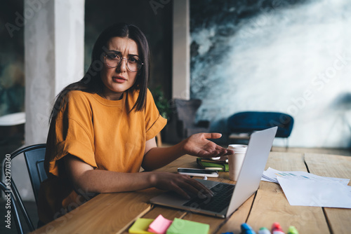 Confused young lady sitting at table with laptop photo