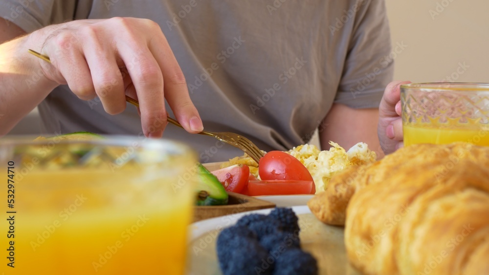 Spying on a man who has breakfast. A man in casual clothes eats a breakfast of eggs with tomatoes and fresh avocado and drinks orange juice. American breakfast with lots of calories.