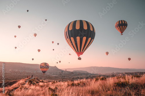 Colorful hot air balloons. Popular tourist attraction - sunrise watching in Cappadocia. Scenic view over autumn orange grass field. Amazing natural summer morning scenery. Best famous travel location