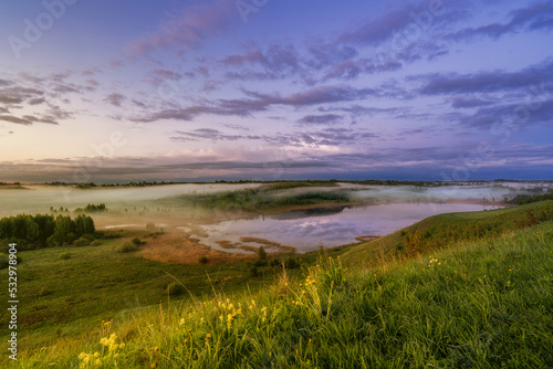 A landscape with green meadow under blue sky, small lake, cloud sky refclecting in the lake, on sunset