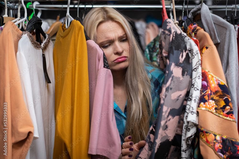 A sad blonde woman shopping in a clothing store.