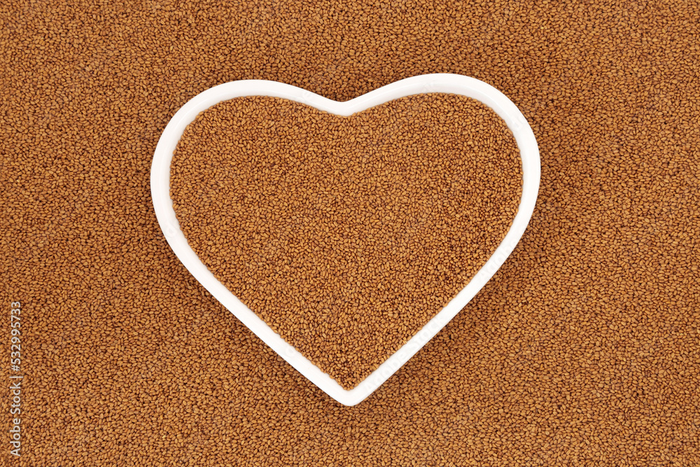 Camelina seed for good heart health. Highly nutritious healthy food reduces LDL levels for low cholesterol  cardiovascular benefits. Background with white heart shaped dish, flat lay, top view.