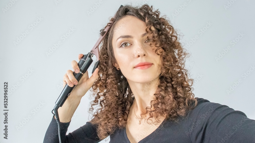 Curly hair. Beautiful brunette woman with curly hair, curls her hair, uses curling tongs to get fine curls. Hairstyles and hairdressing tools. Curly hair. Beautiful brunette woman with curly hair, curls her hair, uses curling tongs to get fine curls. Hairstyles and hairdressing tools.
