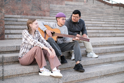 Group of milenial people walking, having fun together  outdoor. Group of high school teens play guitar and listen to music. Multiethnic millenial friends spend free time together.  #532998131