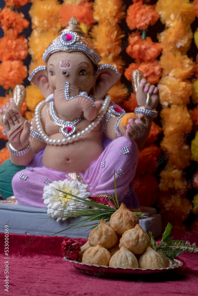 A Beautiful clay statue/Idol of an Indian god Lord Ganesha decorated with colourful Marigold garland 