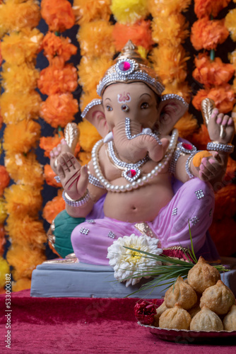 A Beautiful clay statue Idol of an Indian god Lord Ganesha decorated with colourful Marigold garland 