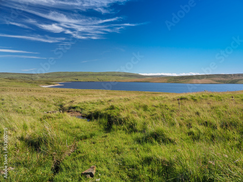Cow Green Reservoir and dam, on the River Tees, under blue sky and white wispy clouds, North Pennines, UK