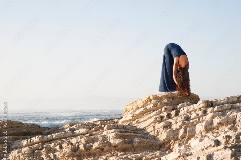 Woman folding forward in Yoga Pose by the sea.