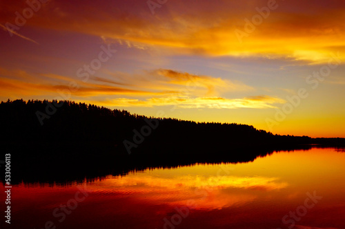 Fototapeta Naklejka Na Ścianę i Meble -  Wild nature, picturesque water landscape. Coniferous forest and red sunset sky are reflected in the water, ripples and waves on the water. Calm quiet evening, harmony. background, wallpaper, postcard