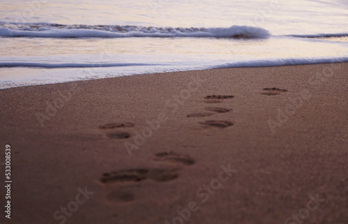 footprints on the beach waves at sunset