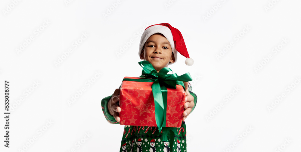 Gift for you. Happy smiling child in a knitted colorful sweater holds box in festive package. Boy rejoices at holiday, Christmas, New Year.