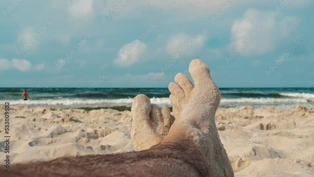 Caucasian Male Enjoying Sun Bath Sitting on Seashore Beach With Sand on Feet Caucasian Male Enjoying Sun Bath Sitting on Seashore Beach With Sand on Feet