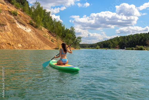 Young beautiful woman in blue bikini is riding on sup board by the Dzerzhinsky quarries