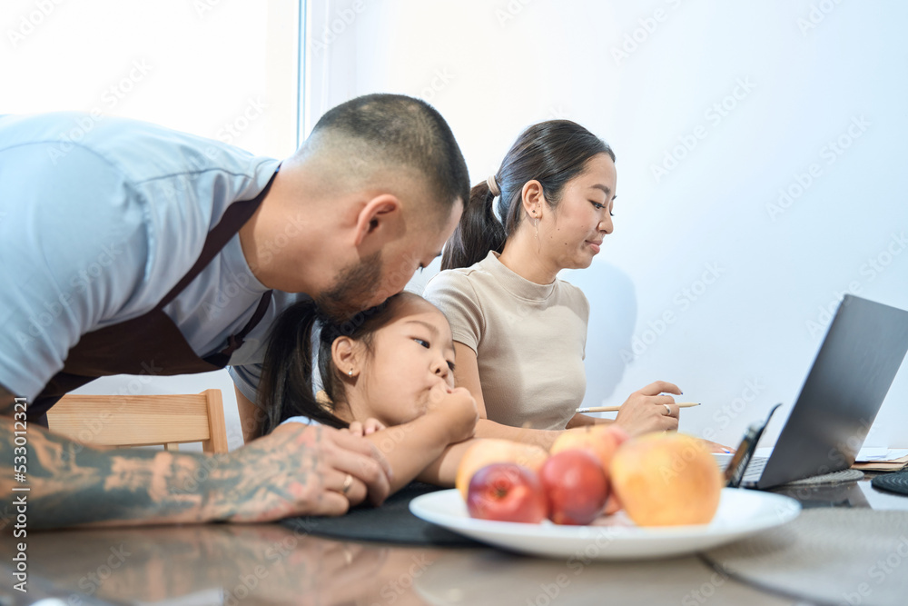 Kind dad kisses his daughter on head, next laptop mom Kind dad kisses his daughter on head, next laptop mom