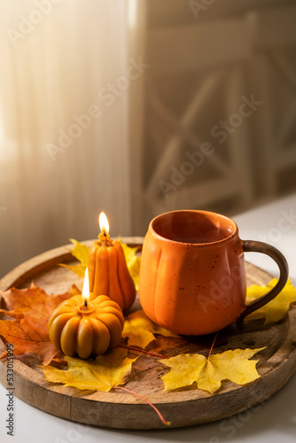 A cup of tea, candles and autumn leaves on a wooden tray.