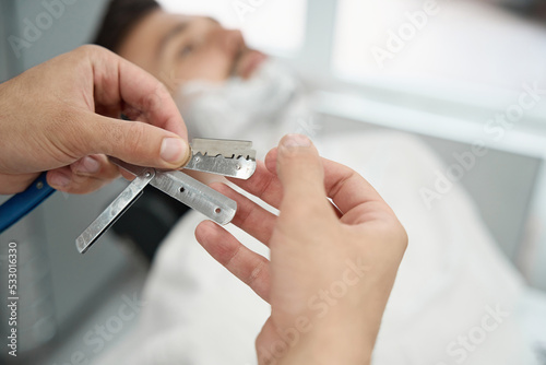 Careful barber getting ready to shave guest face with straight razor