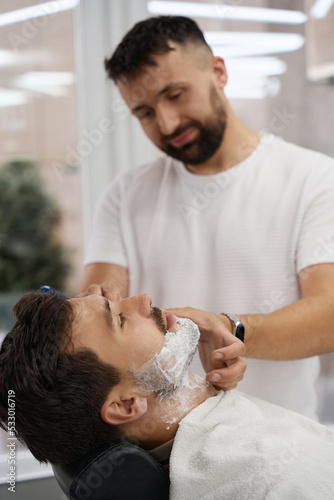 Young brunet man having his face shaved at hair salon