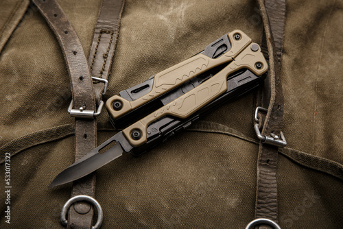 Modern multitool with many tools. A portable multitasking tool on a vintage canvas backpack. Dark back. photo