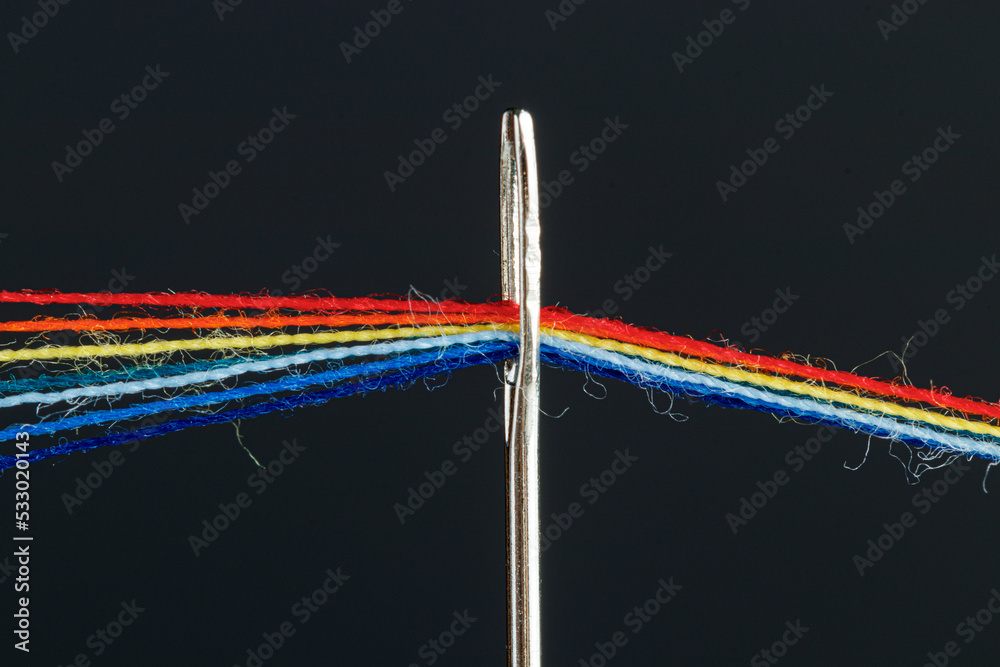 multi-colored threads for sewing in the form of a rainbow pass through an antique needle on a black background