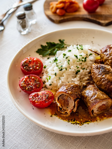 Wrapped pork served with white rice and cherry tomatoes on white table