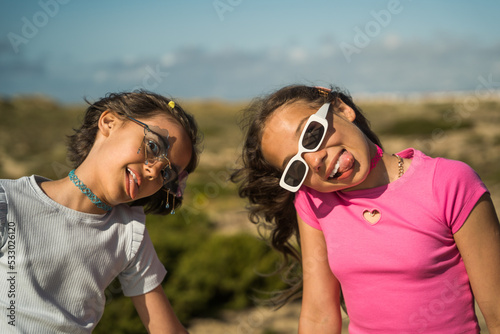 Two child girls making funny faces and having fun together while playing outside
