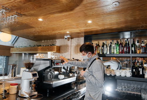 A masked barista prepares an exquisite delicious coffee at the bar in a coffee shop. The work of restaurants and cafes during the pandemic.