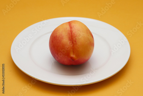 Nectarine in a white plate on an orange background. Shallow depth of field