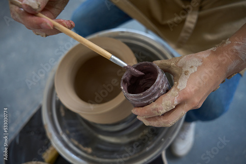 Potter sits potter wheel with paint and brush in his hands