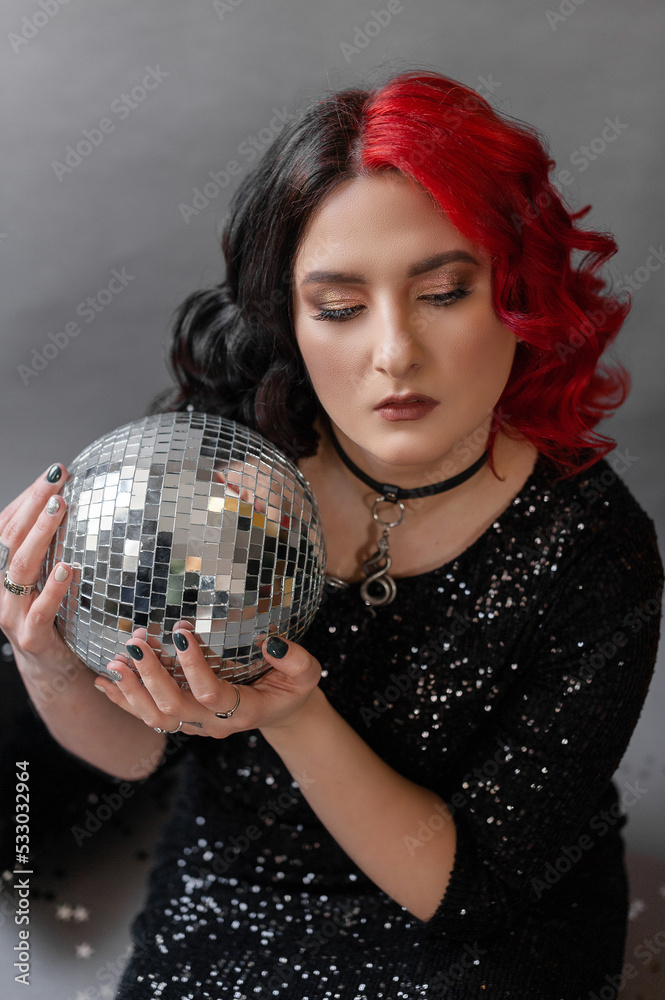 a girl with one half red hair the other black in a black tight dress with sequins for her birthday for a holiday in the studio on a gray background with golden black balloons with disco ball a girl with one half red hair the other black in a black tight dress with sequins for her birthday for a holiday in the studio on a gray background with golden black balloons with disco ball